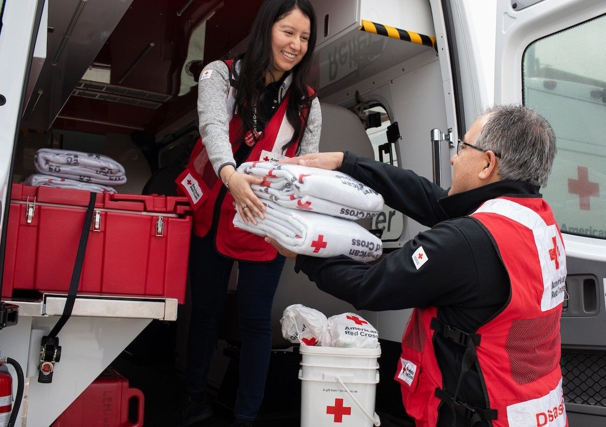Two Red Cross Disaster volunteers are unloading supplies from an emergency response vehicle.