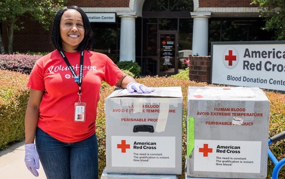 Red Cross Blood Services volunteer stands next to blood products she is helping to transport.