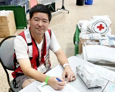 Man in Red Cross vest sitting at a table in a Red Cross shelter