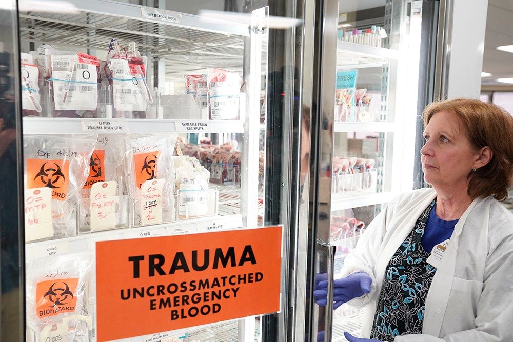 woman opening cooler with sign on it that says "Trauma. Uncrossmatched emergency blood", filled with blood products